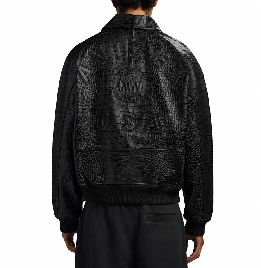 Black Avirex crocodile-texture leather jacket modeled from the back, featuring raised AVIREX USA lettering and classic bomber-style ribbed hem.