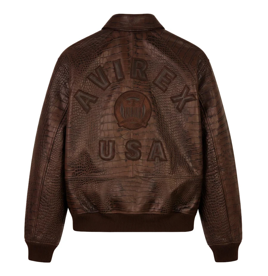 Back view of a brown crocodile-effect bomber jacket on a white background, featuring large AVIREX USA lettering, a central emblem and ribbed hem.