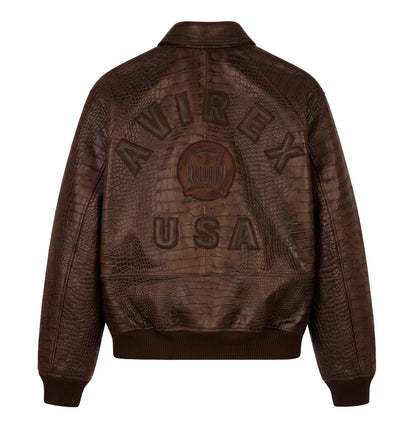 Back view of a brown crocodile-effect bomber jacket on a white background, featuring large AVIREX USA lettering, a central emblem and ribbed hem.