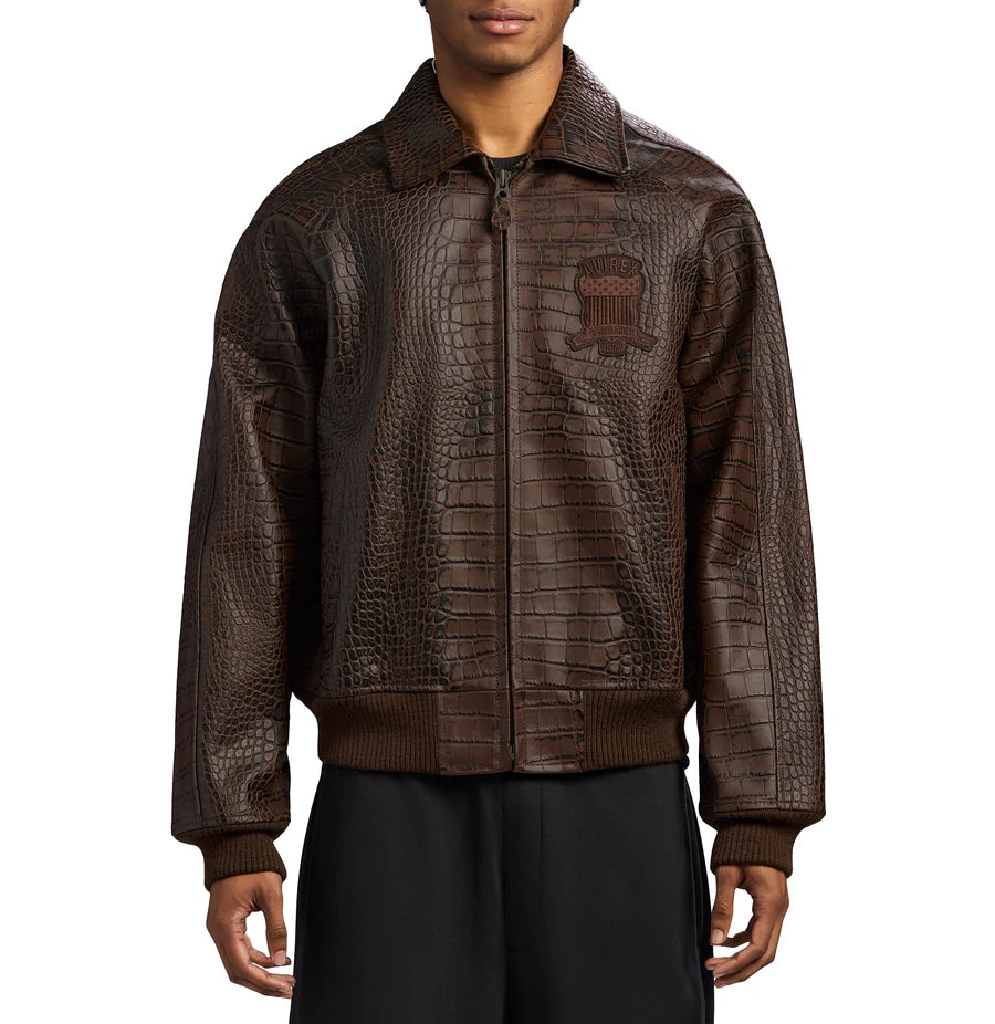 Front view of a men's brown crocodile-texture bomber jacket featuring a zip closure, pointed collar, chest emblem and ribbed cuffs, showcasing vintage-inspired streetwear style.