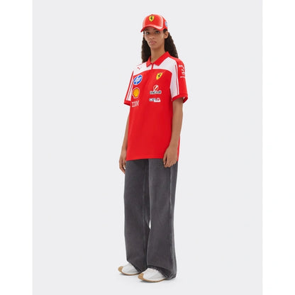 A model wearing a red and white Ferrari polo shirt with various sponsor logos, a matching red cap, and dark gray wide-leg jeans, standing against a light gray background.
