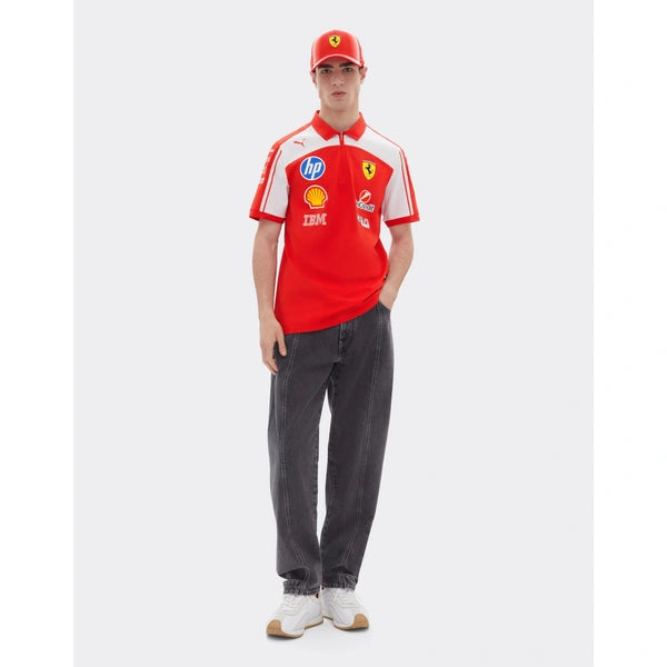 A man modeling a red and white Scuderia Ferrari short-sleeve polo shirt with various sponsor logos, paired with dark gray jeans, a red Scuderia Ferrari cap, and white sneakers, set against a plain light gray background.