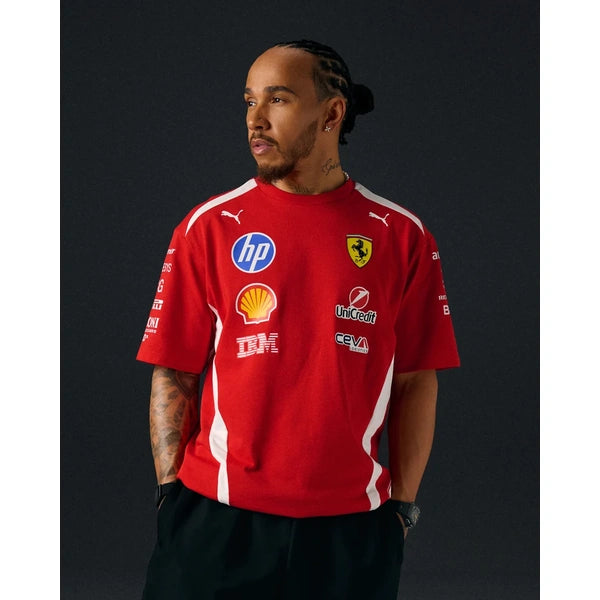 A man wearing a red Ferrari short-sleeve sports jersey with white stripes and multiple sponsor logos, including HP, Shell, and IBM, posed against a dark studio background.