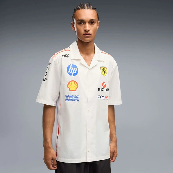 A model wearing a white short-sleeve button-up shirt with Ferrari and Puma branding, featuring sponsor logos including HP, Shell, and IBM, set against a gray studio background.