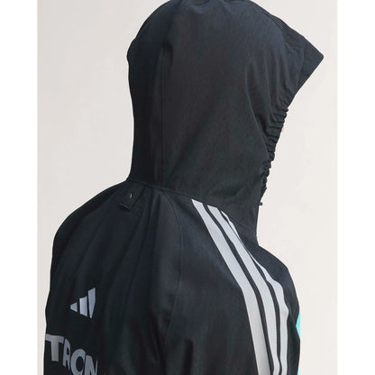 Close-up side view of a black Adidas hooded jacket with white three-stripe detailing on the shoulder and sleeve, shown against a light neutral background.