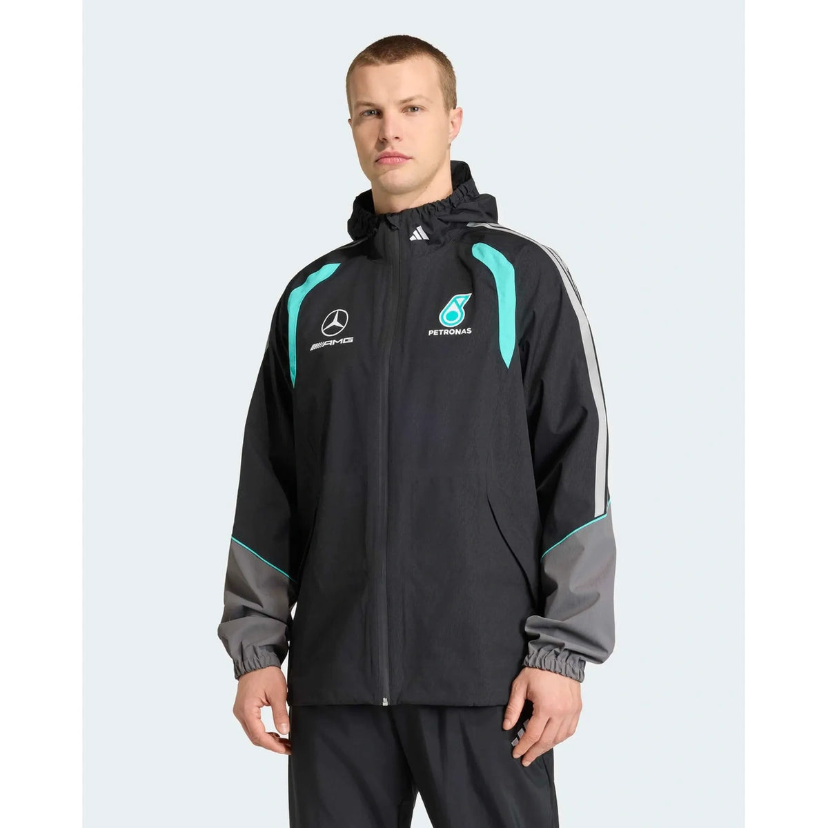 A man wearing a black Mercedes Petronas team jacket with teal and gray accents, featuring the Mercedes star logo and Petronas sponsor logo on the chest, set against a light gray background.