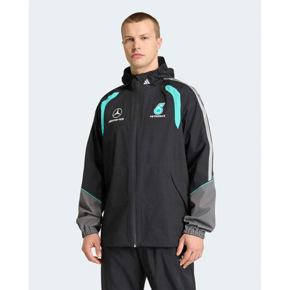 A man wearing a black Mercedes Petronas team jacket with teal and gray accents, featuring the Mercedes star logo and Petronas sponsor logo on the chest, set against a light gray background.