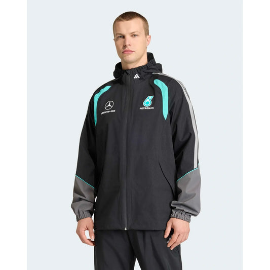 A man wearing a black Mercedes Petronas team jacket with teal and gray accents, featuring the Mercedes star logo and Petronas sponsor logo on the chest, set against a light gray background.