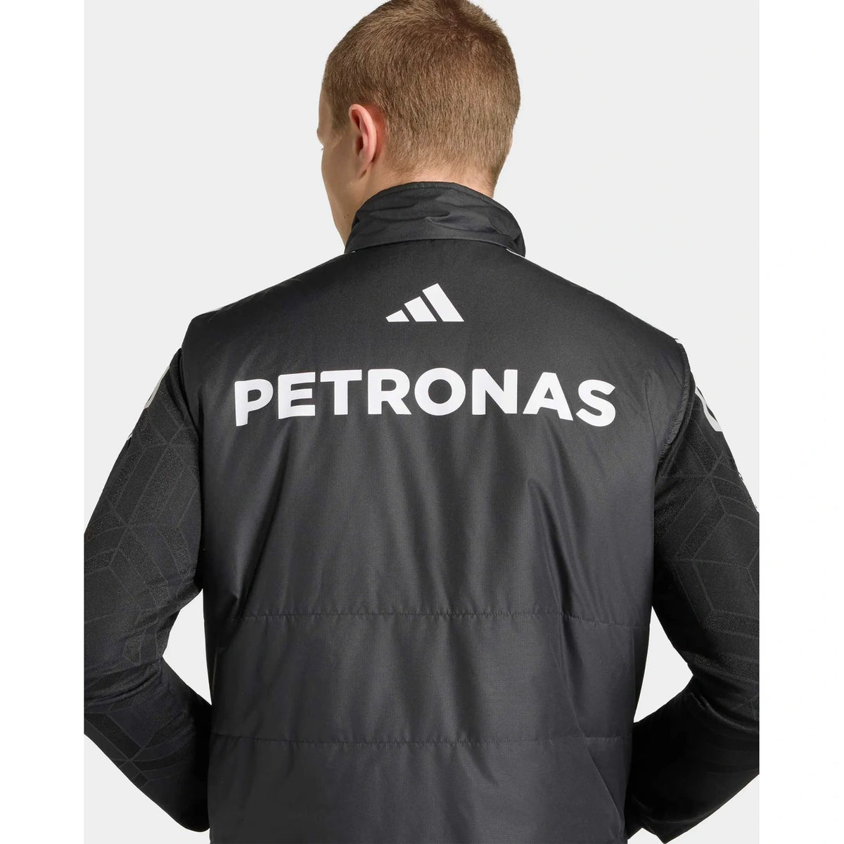 Rear view of a man wearing a black Adidas jacket with large white PETRONAS branding on the back, against a light gray background.