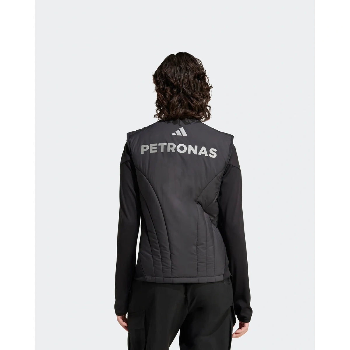 A person shown from the back wearing a black Adidas Petronas athletic jacket with white branding on the back, set against a light gray studio background.
